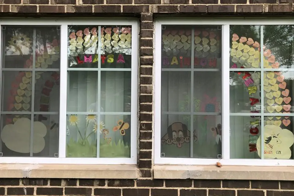 Two adjacent windows display colorful paper rainbows, clouds, butterflies, and flowers, with messages and hearts arranged on the glass panes.