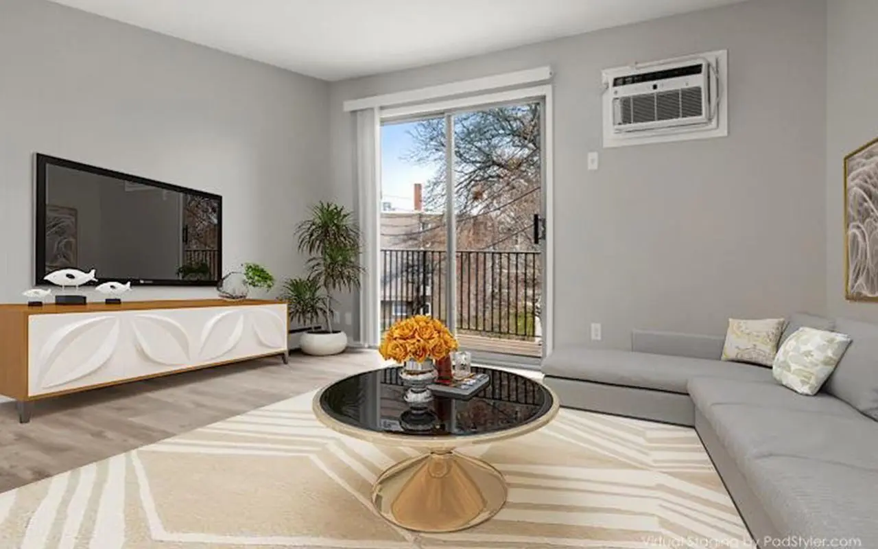Modern living room with a gray sectional sofa, round coffee table, TV on a console, indoor plants, and a sliding glass door leading to a balcony.