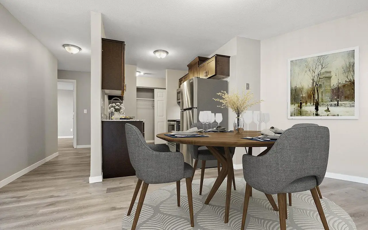 Modern kitchen and dining area with a round table set for four, gray chairs, stainless steel appliances, and a large framed artwork on a light-colored wall.
