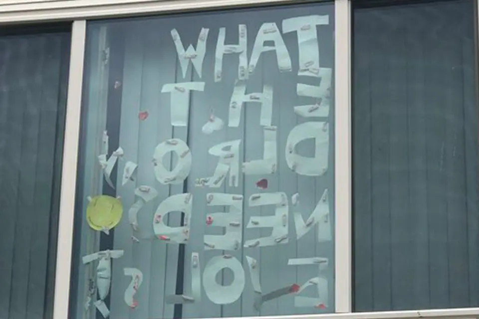 Paper cut-out letters taped inside a window read “WHAT DO YOU NEED?” in reverse, with some small decorations attached to the glass.