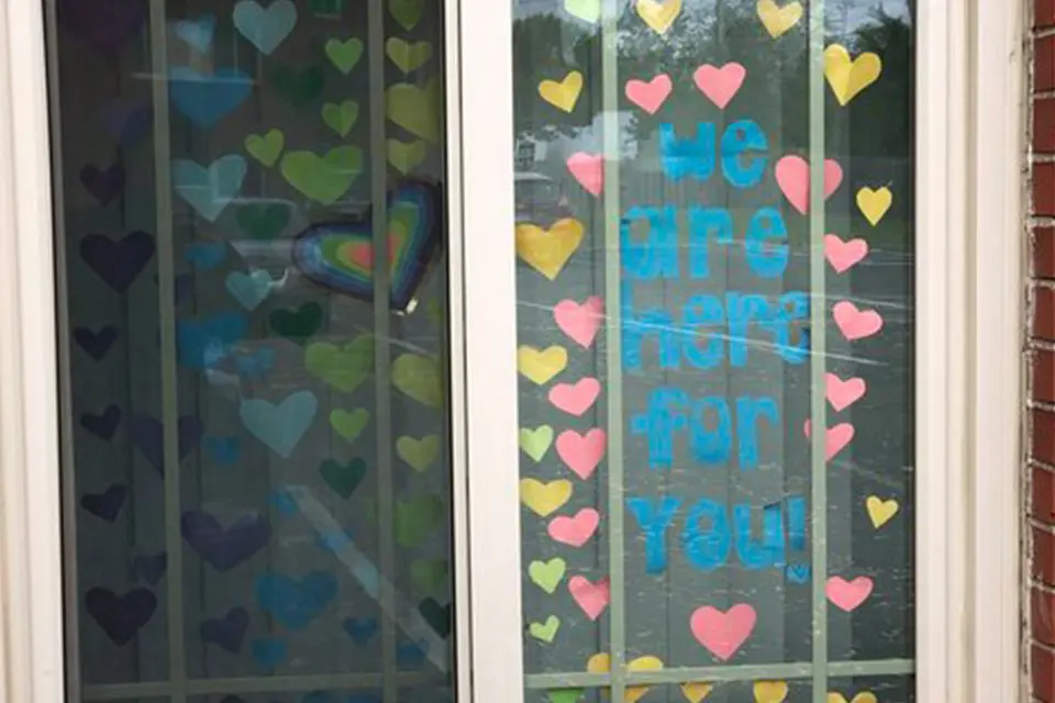 A window decorated with colorful paper hearts and the words "we are here for you!" written in blue letters.