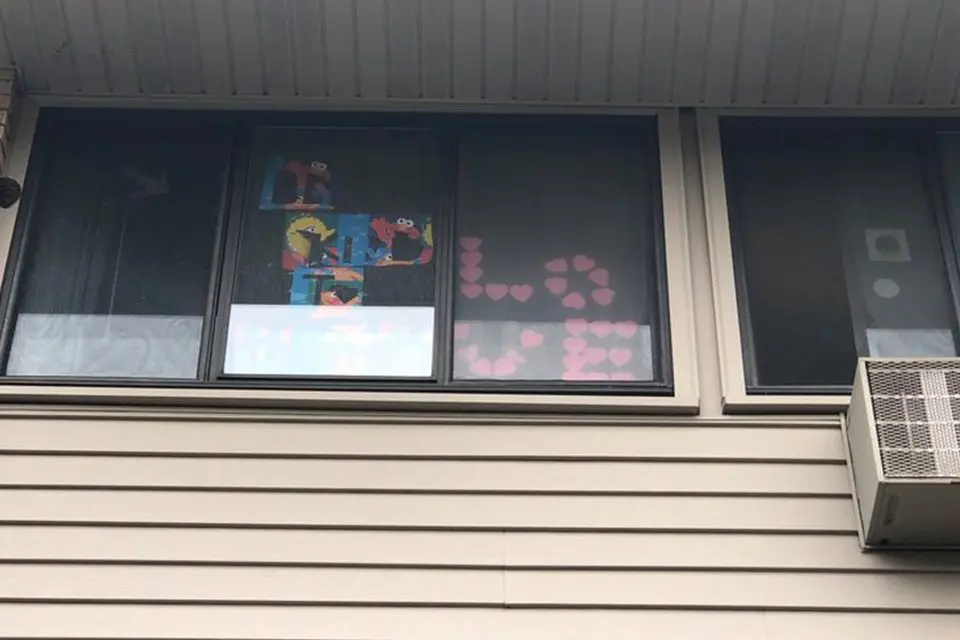A window displays colorful post-it note art, including cartoon characters and pink heart shapes forming the letters "LA." An air conditioning unit is installed below the window.