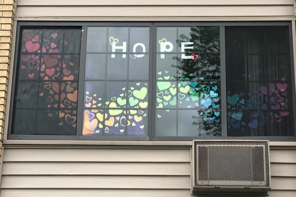 A window displays the word "HOPE" and numerous colorful heart cutouts arranged in a rainbow pattern, with an air conditioning unit below the window.