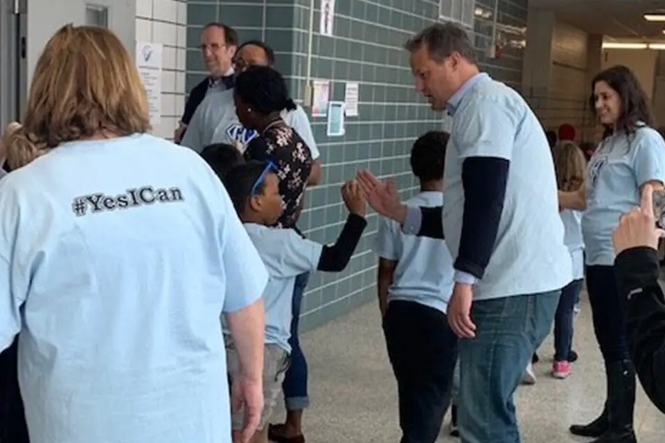 Adults wearing matching "#YesICan" shirts give high fives to young children in a school hallway.