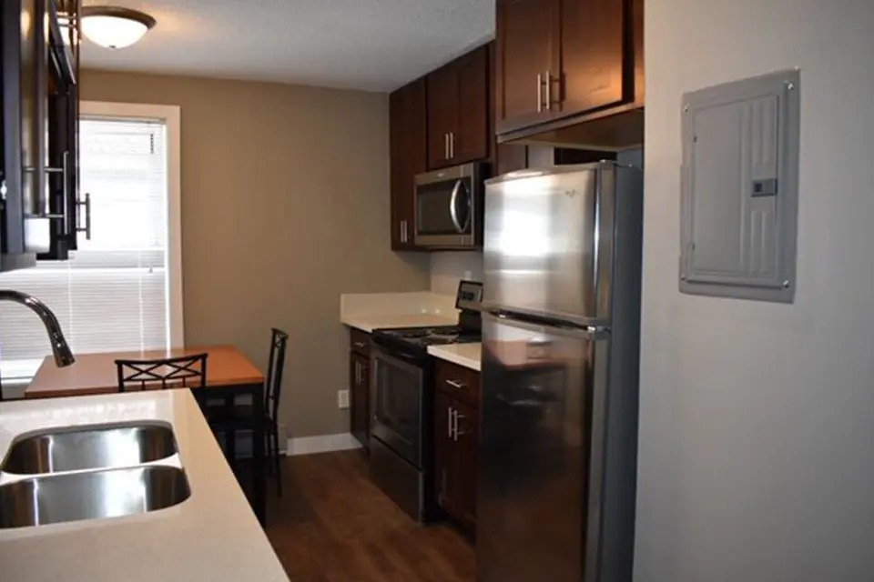 Modern kitchen with dark wood cabinets, stainless steel appliances, a double sink, small dining table, and a window providing natural light.