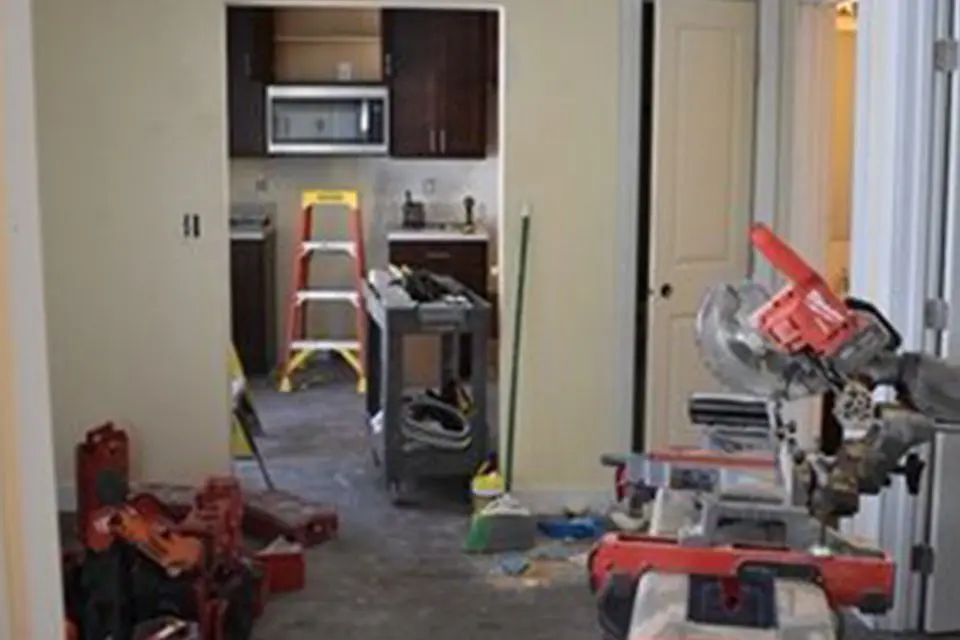 A home kitchen under renovation with tools, a ladder, and construction equipment scattered across the floor.