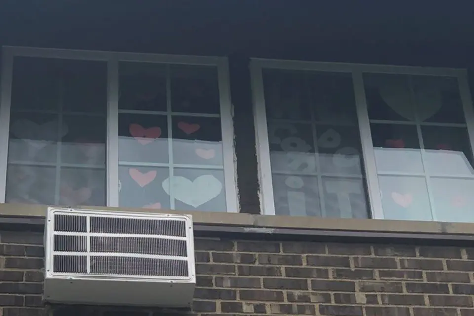 Two building windows display paper cutouts of hearts and a panda, with an air conditioning unit installed below the windows.