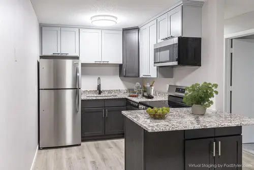 Modern kitchen with stainless steel appliances, gray cabinets, granite countertops, and a kitchen island with a bowl of apples and a potted plant.