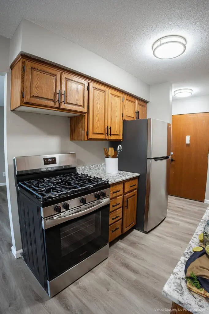 A modern kitchen with wooden cabinets, a stainless steel gas stove, a matching refrigerator, and light wood flooring under bright ceiling lights.