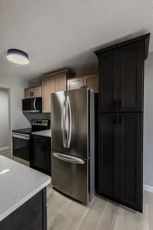 Modern kitchen with stainless steel refrigerator, black stove, light and dark cabinets, and light wood flooring.