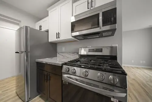 A modern kitchen with stainless steel refrigerator, gas stove, and microwave, white upper cabinets, black lower cabinets, and marble-look countertop.