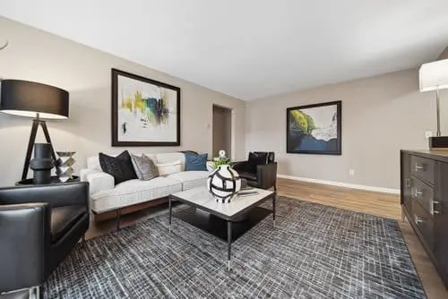 Modern living room with a white sofa, black armchairs, abstract wall art, a patterned rug, and a central coffee table with a decorative object.