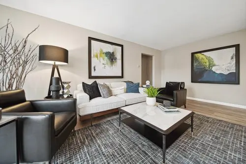 Modern living room with a white sofa, black armchairs, a coffee table, abstract wall art, a floor lamp, and decorative branches on a patterned rug.