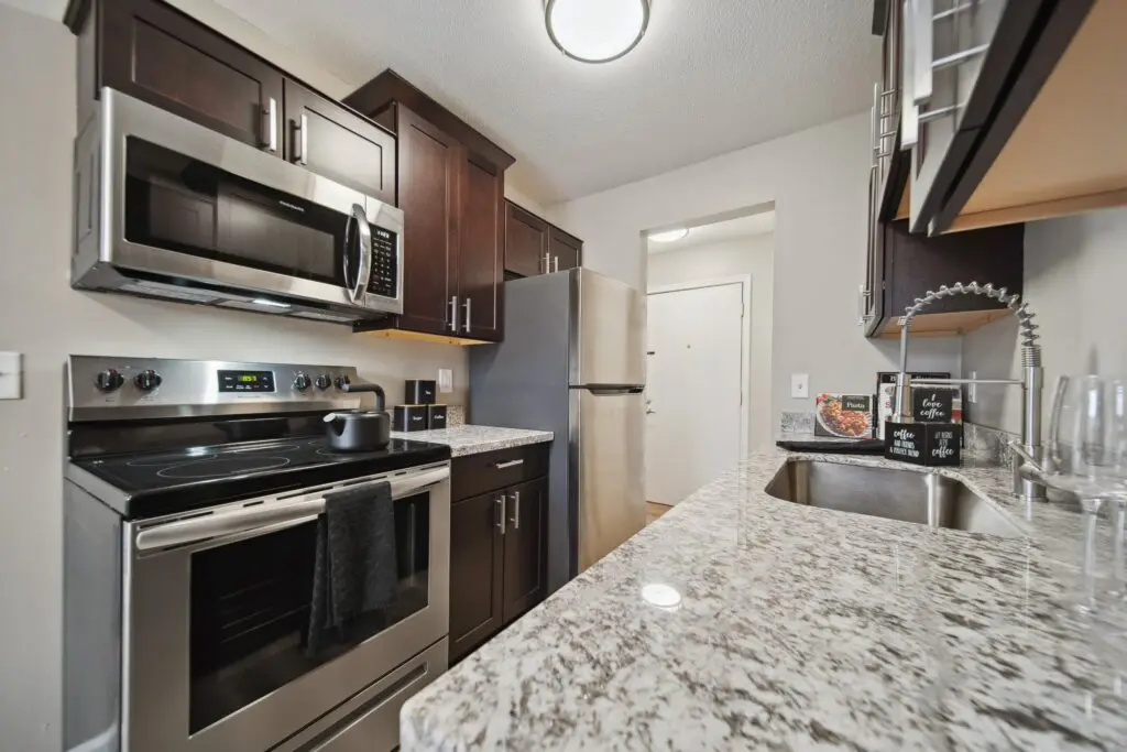 Modern kitchen with stainless steel appliances, dark cabinets, granite countertops, and a sink with a drying rack; a pot sits on the stove and a towel hangs on the oven door.
