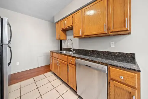 A kitchen with wooden cabinets, granite countertops, stainless steel appliances, a sink, and tile flooring.