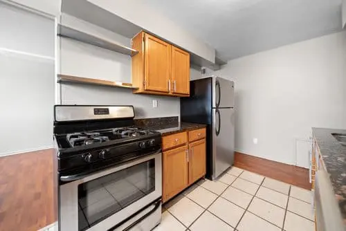 Modern kitchen with stainless steel gas stove and refrigerator, wood cabinets, open shelves, granite countertops, and tile flooring.