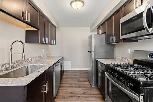 Modern galley kitchen with dark cabinets, stainless steel appliances, granite countertops, and a wood floor.