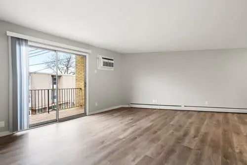 Empty room with light gray walls, wood-style flooring, a wall-mounted air conditioner, and a glass sliding door leading to a small balcony.