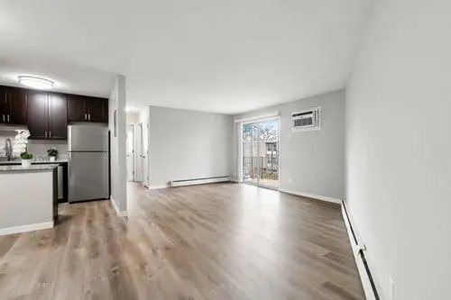 Unfurnished apartment with wood flooring, white walls, a kitchen with stainless steel appliances, and a sliding glass door leading to a balcony.