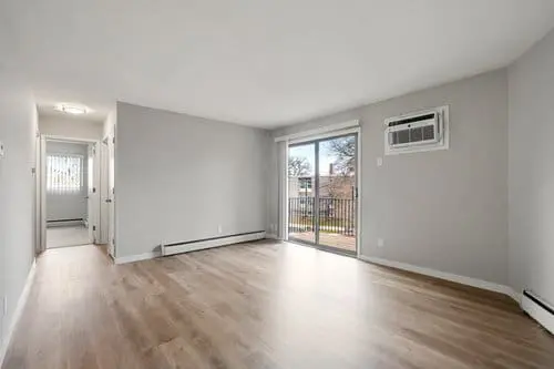 Empty living room with light wood flooring, gray walls, a wall-mounted air conditioner, sliding glass doors, and a view of an outdoor balcony.
