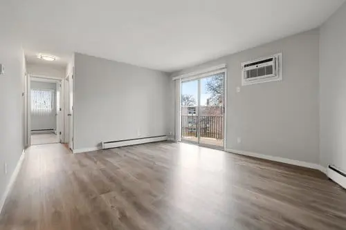 Empty living room with light gray walls, wood-look flooring, a wall-mounted air conditioner, and sliding glass doors leading to a balcony.