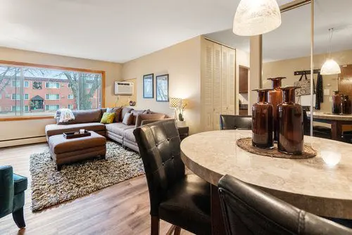 Modern living and dining area with a brown sectional sofa, dining table with dark chairs, large window, and neutral decor.