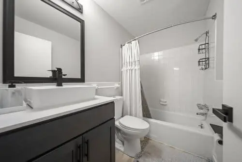 Modern bathroom with a white bathtub and shower, a white sink with black fixtures, a toilet, and a large mirror above the vanity.