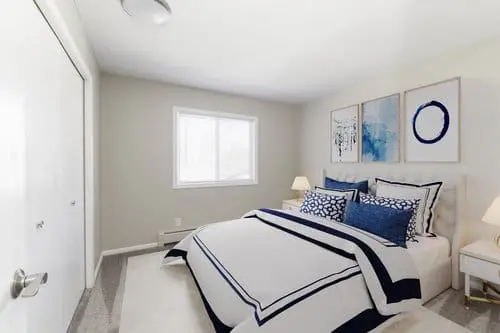 A bedroom with a neatly made bed featuring blue and white bedding, two bedside tables with lamps, and three abstract paintings above the headboard.