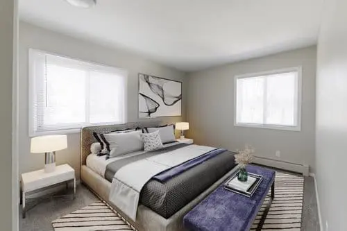 A modern bedroom with a large bed, two side tables with lamps, abstract wall art, a cushioned bench, and two windows letting in natural light.
