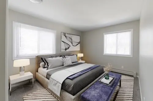 Modern bedroom with a large bed, two bedside tables with lamps, a bench at the foot of the bed, abstract wall art, and two windows letting in natural light.