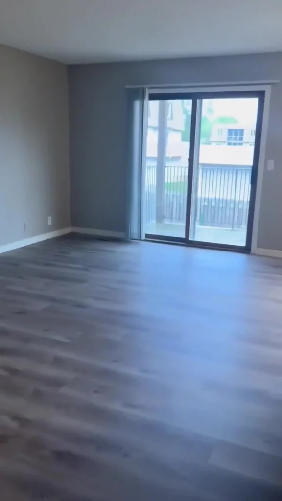 Empty room with gray walls and wood-look flooring, featuring a large sliding glass door that opens to a balcony with a railing outside.